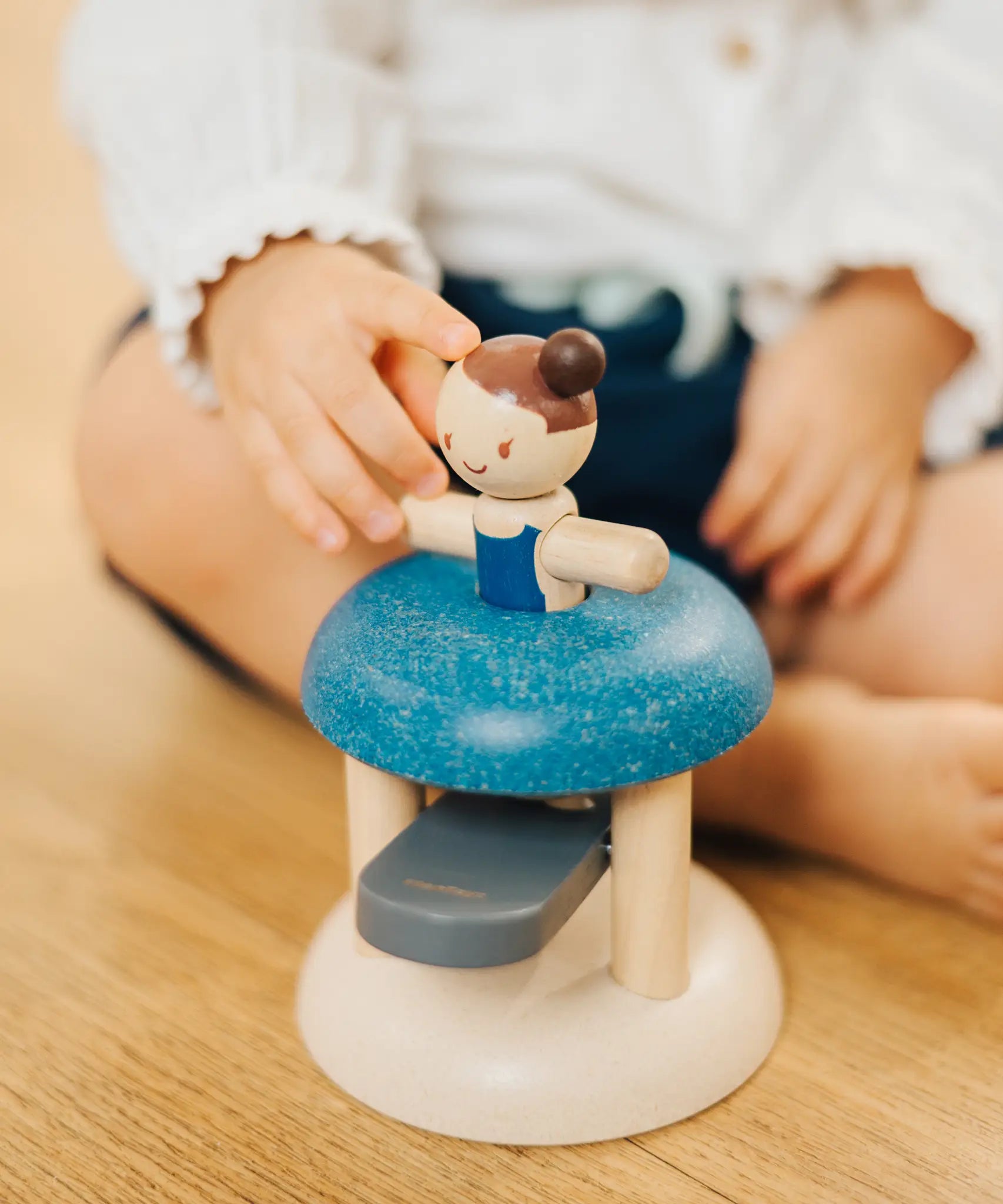 Child pushing the PlanToys gymnast peg doll inside the base ready to be launched