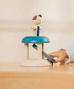 Child's hand pressing down on the base launching the PlanToys gymnast peg doll
