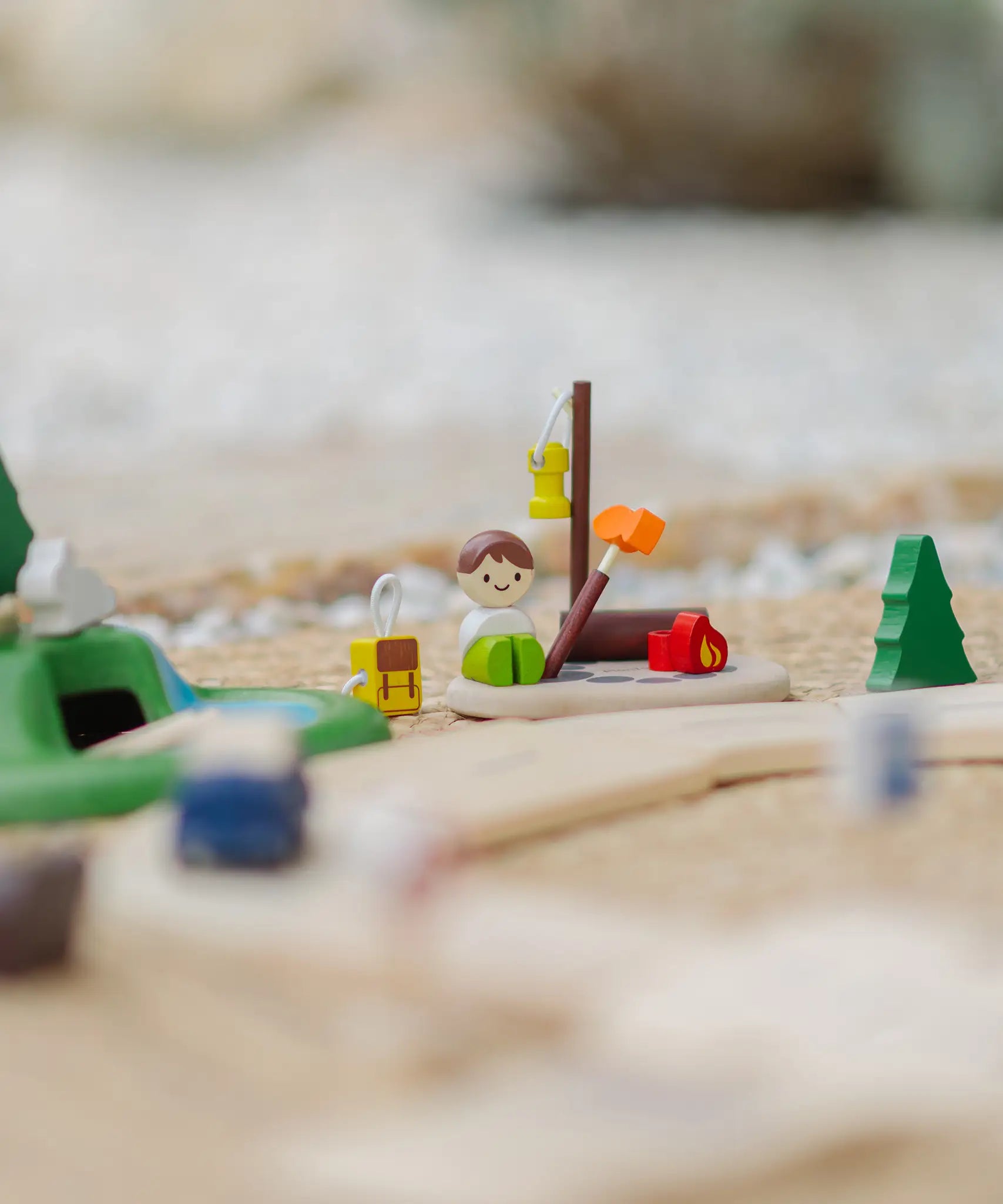 PlanToys wooden jungle explorers road playset showing a camper figure doll sitting next to a backpack and campfire