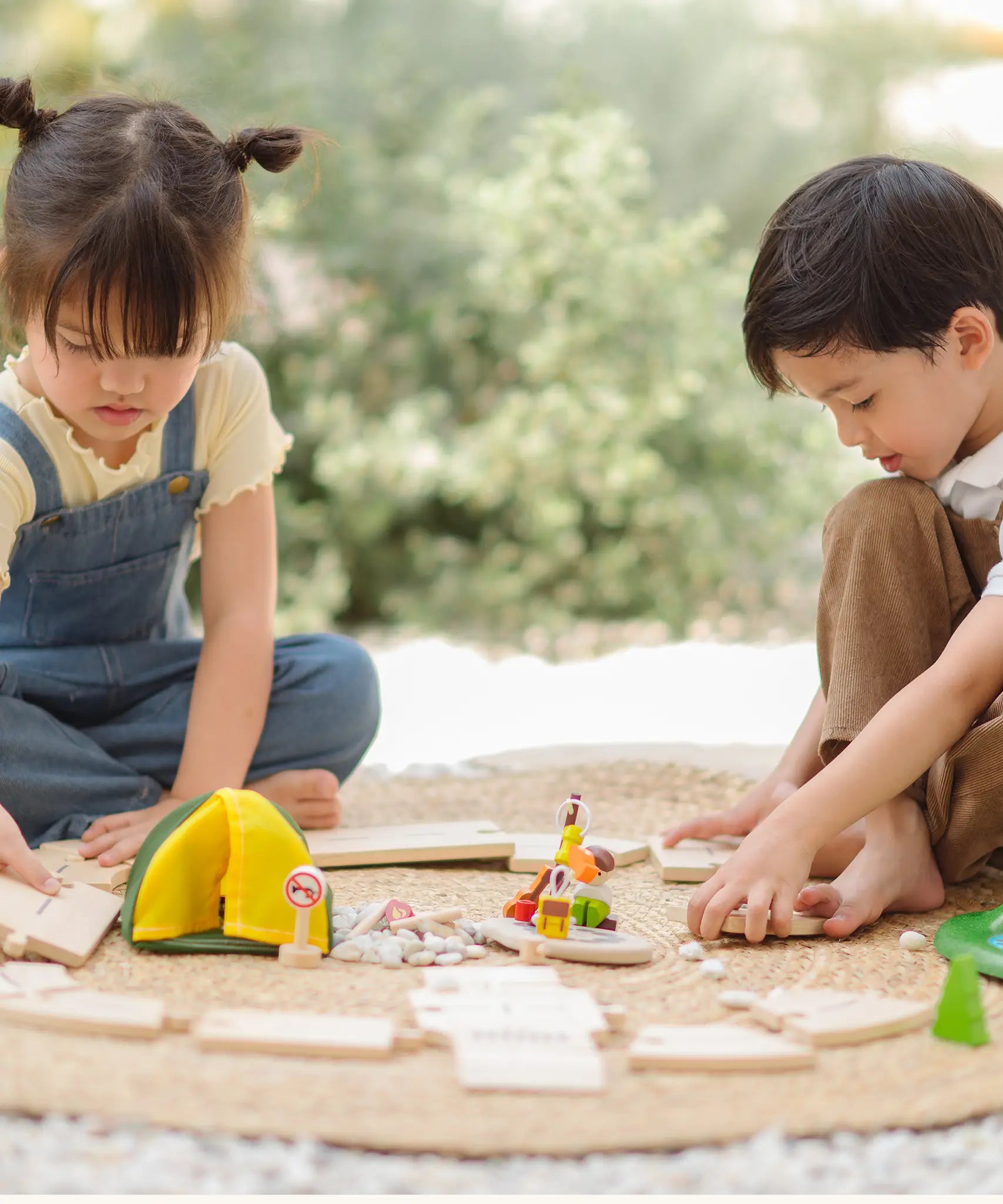 Children assembling road pieces from the PlanToys wooden jungle explorers road playset on a rug in the garden