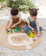 Children playing with the PlanToys wooden jungle explorers road playset on a rug in the garden