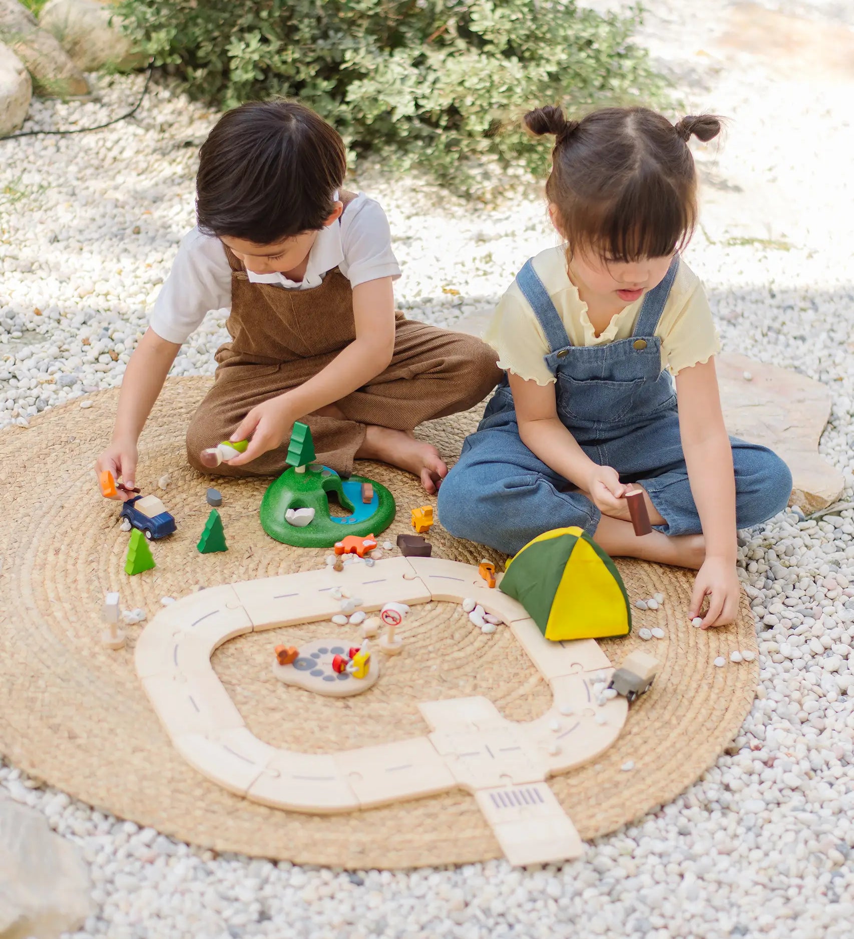 Children playing with the PlanToys wooden jungle explorers road playset on a rug in the garden