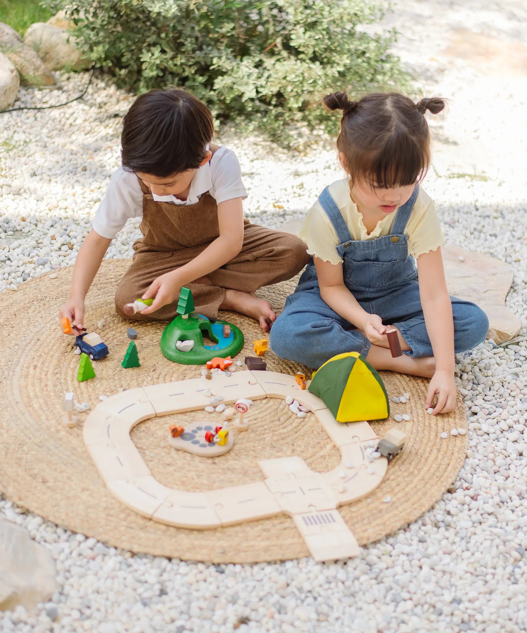 Children playing with the PlanToys wooden jungle explorers road playset on a rug in the garden