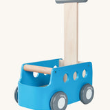 The PlanToys Blue Van Walker is a 2 in 1 toy as a walker and a storage toy box. The van is blue with grey wheels which have "PlanToys" painted onto them, a grey handle with a natural wood section connecting the handle to the van. The image is on a cream background