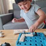 Boy moving the pieces of the Plan Toys plastic free finding penguin family board game on a light wooden table