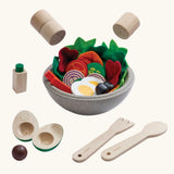 PlanToys little chef's salad set showing  bowl full of wooden playfood standing next to cutlery and salt and pepper shakers hovering above