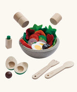PlanToys little chef's salad set showing  bowl full of wooden playfood standing next to cutlery and salt and pepper shakers hovering above
