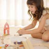 Child sitting next to a PlanToys wooden neighbourhood roadway setup 