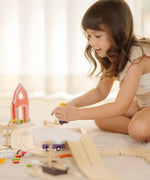 Child sitting next to a PlanToys wooden neighbourhood roadway setup 