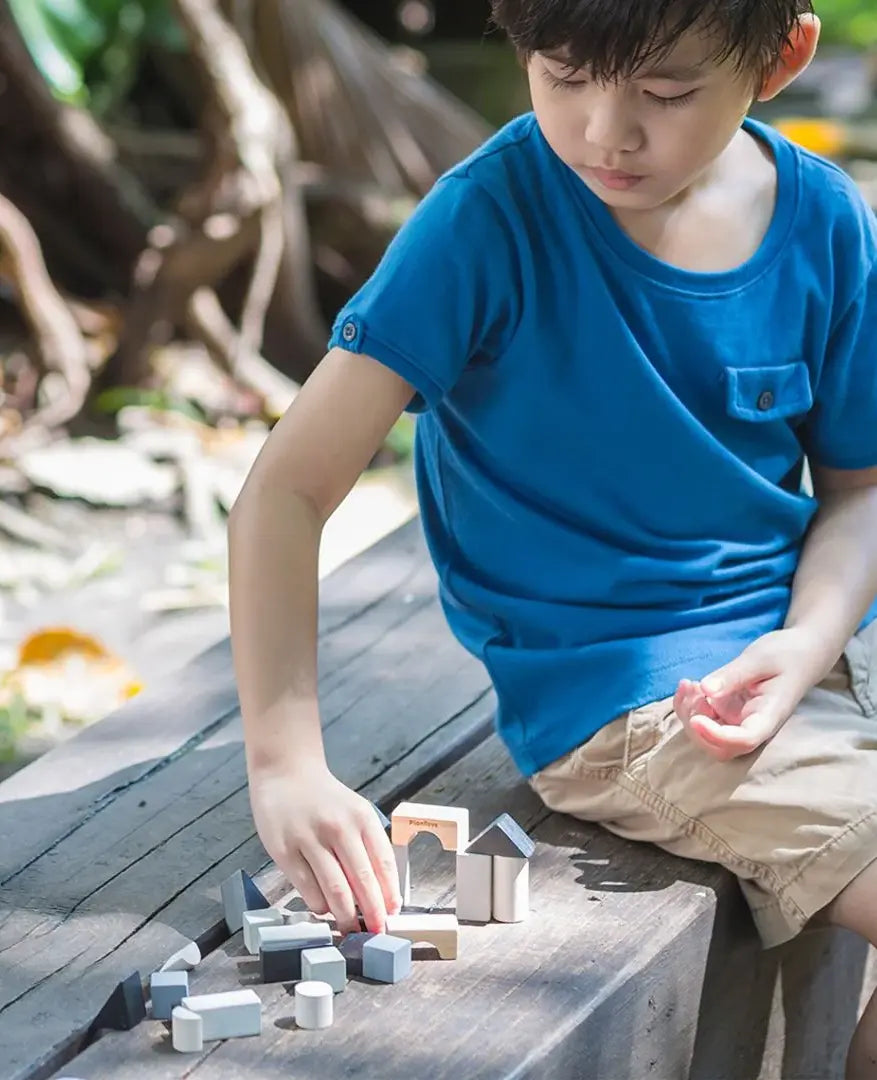 Child playing with small wooden building blocks mini travel set by plantoys outdoors. 