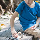 Child playing with small wooden building blocks mini travel set by plantoys outdoors. 
