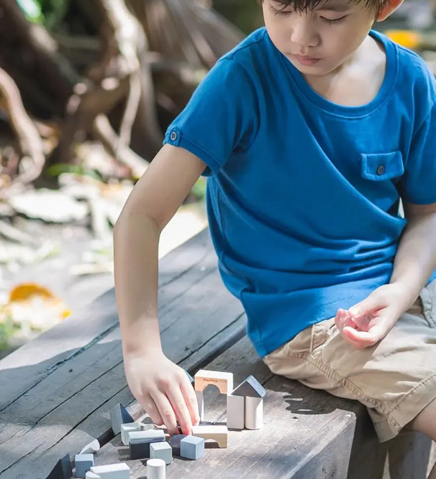 Child playing with small wooden building blocks mini travel set by plantoys outdoors. 