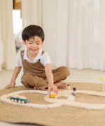 Child playing with the PlanToys my first wooden rail road set holding a yellow suv vehicle 