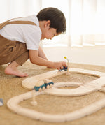 Child playing with the PlanToys my first wooden rail road set holding a blue suv vehicle 
