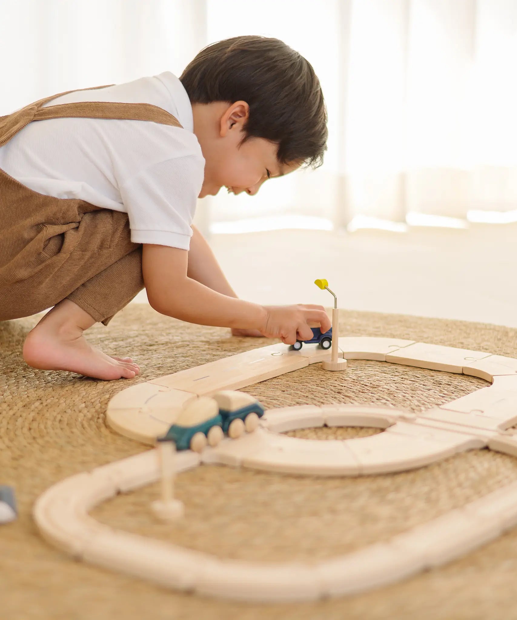 Child playing with the PlanToys my first wooden rail road set holding a blue suv vehicle 