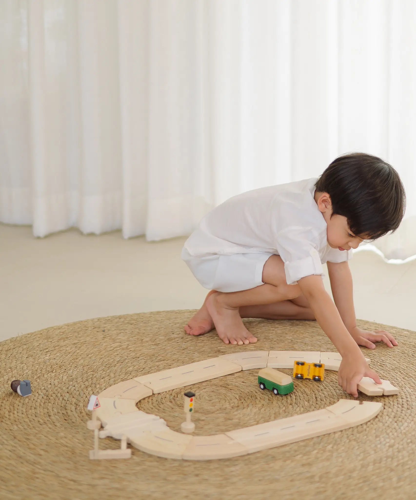 Child building a ring road using the road pieces from the PlanToys my first road way set