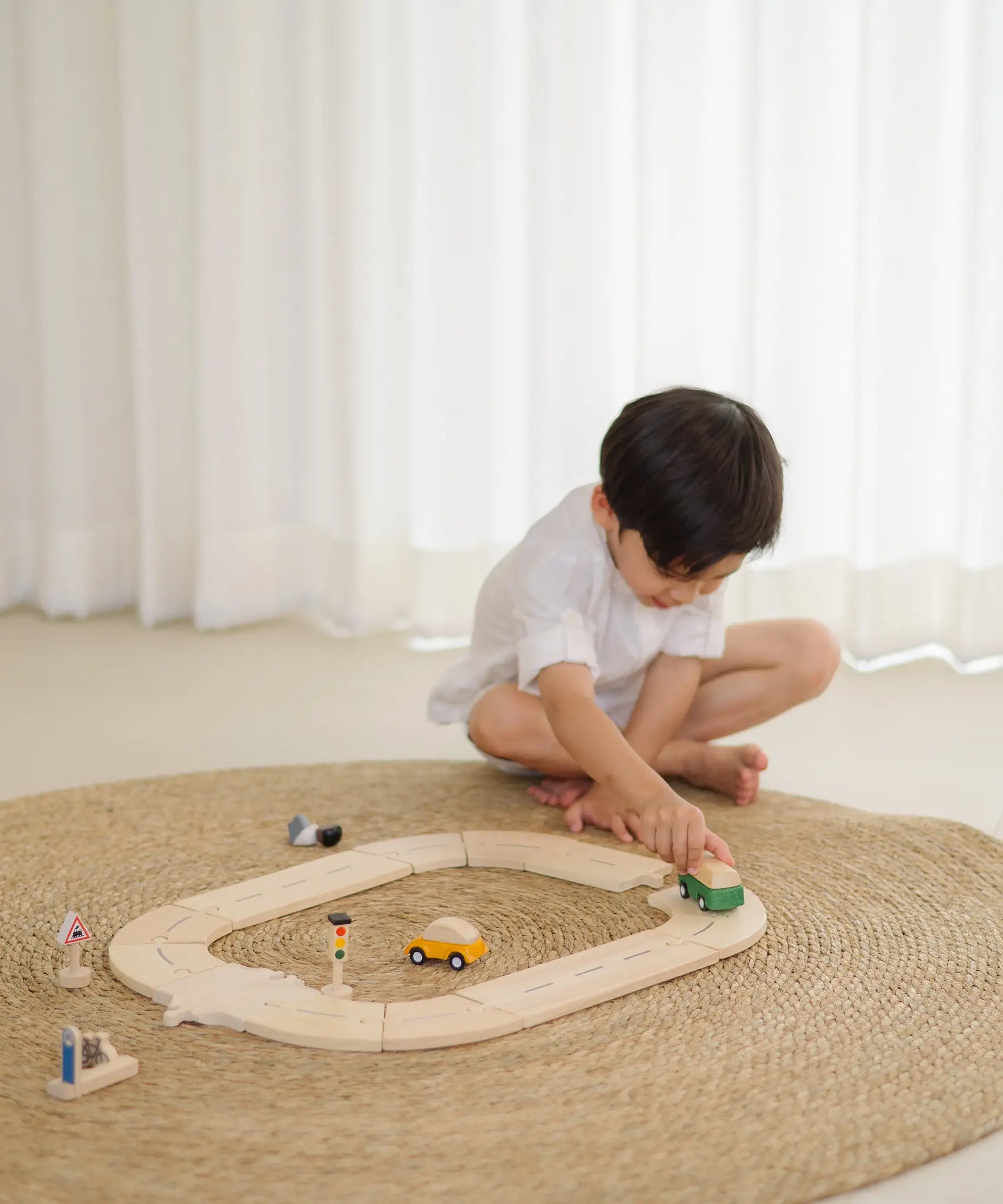 Child holding a green vehicle playing on the PlanToys my first roadway set 