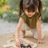 Child pushing a train on wooden rails from the PlanToys my first train set on a woven rug in the garden