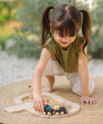 Child pushing a train on wooden rails from the PlanToys my first train set on a woven rug in the garden