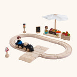 A PlanToys my first train set showing a market stall set standing next to the wooden rails