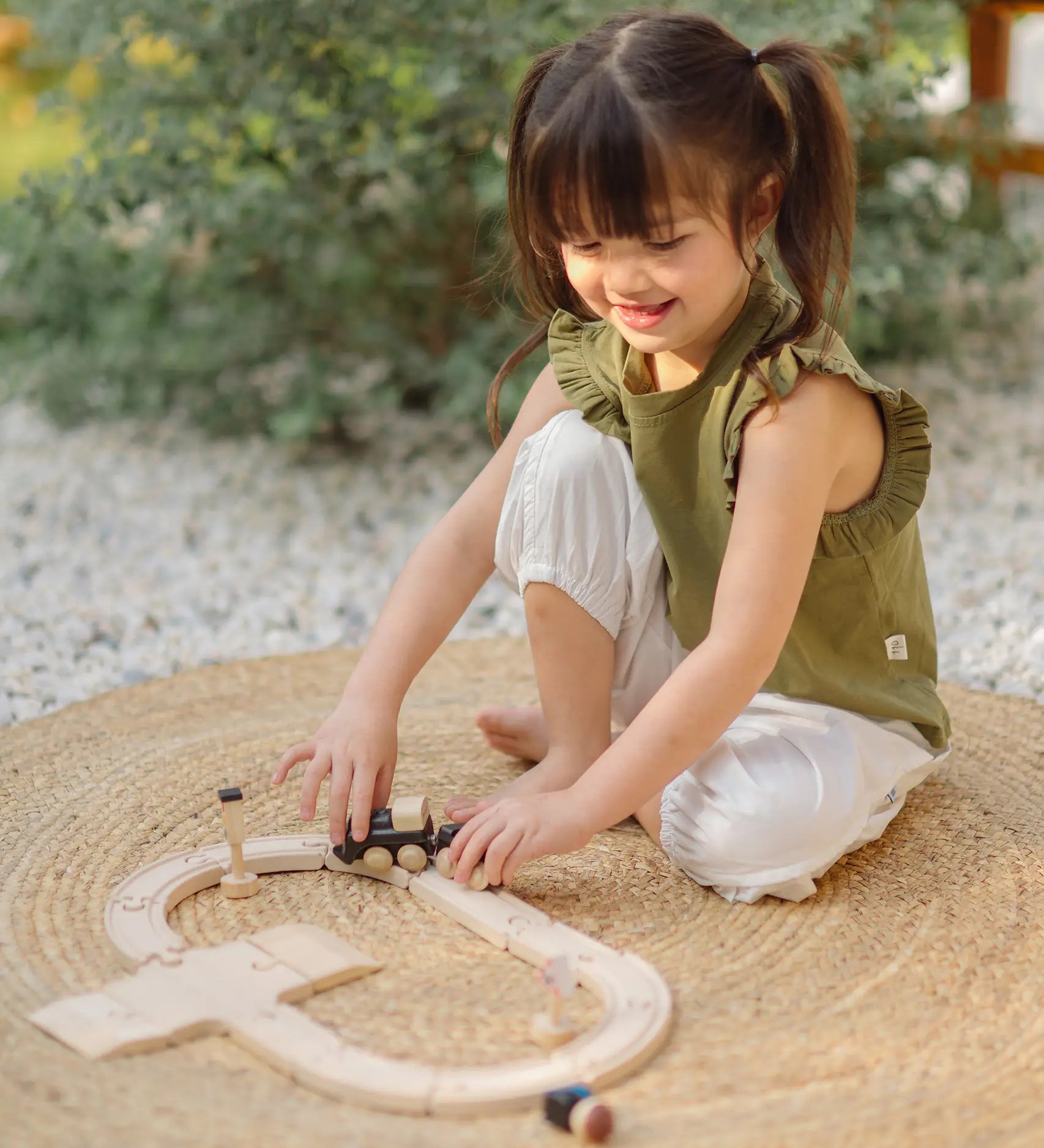 Child playing with the PlanToys my first train set on a woven rug in the garden