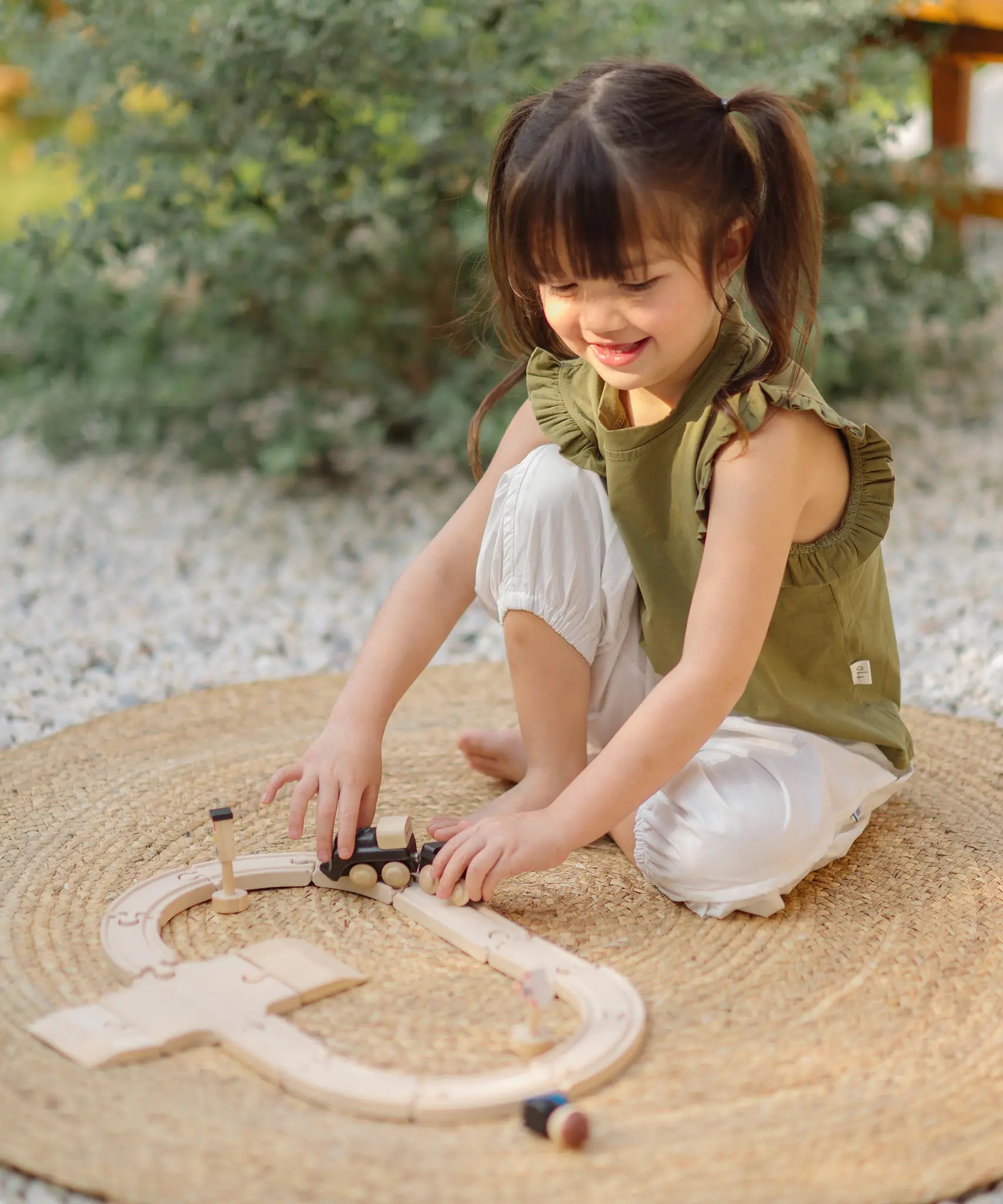 Child playing with the PlanToys my first train set on a woven rug in the garden