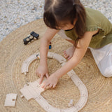 Child assembling wooden rail pieces from the PlanToys my first train set on a woven rug in the garden