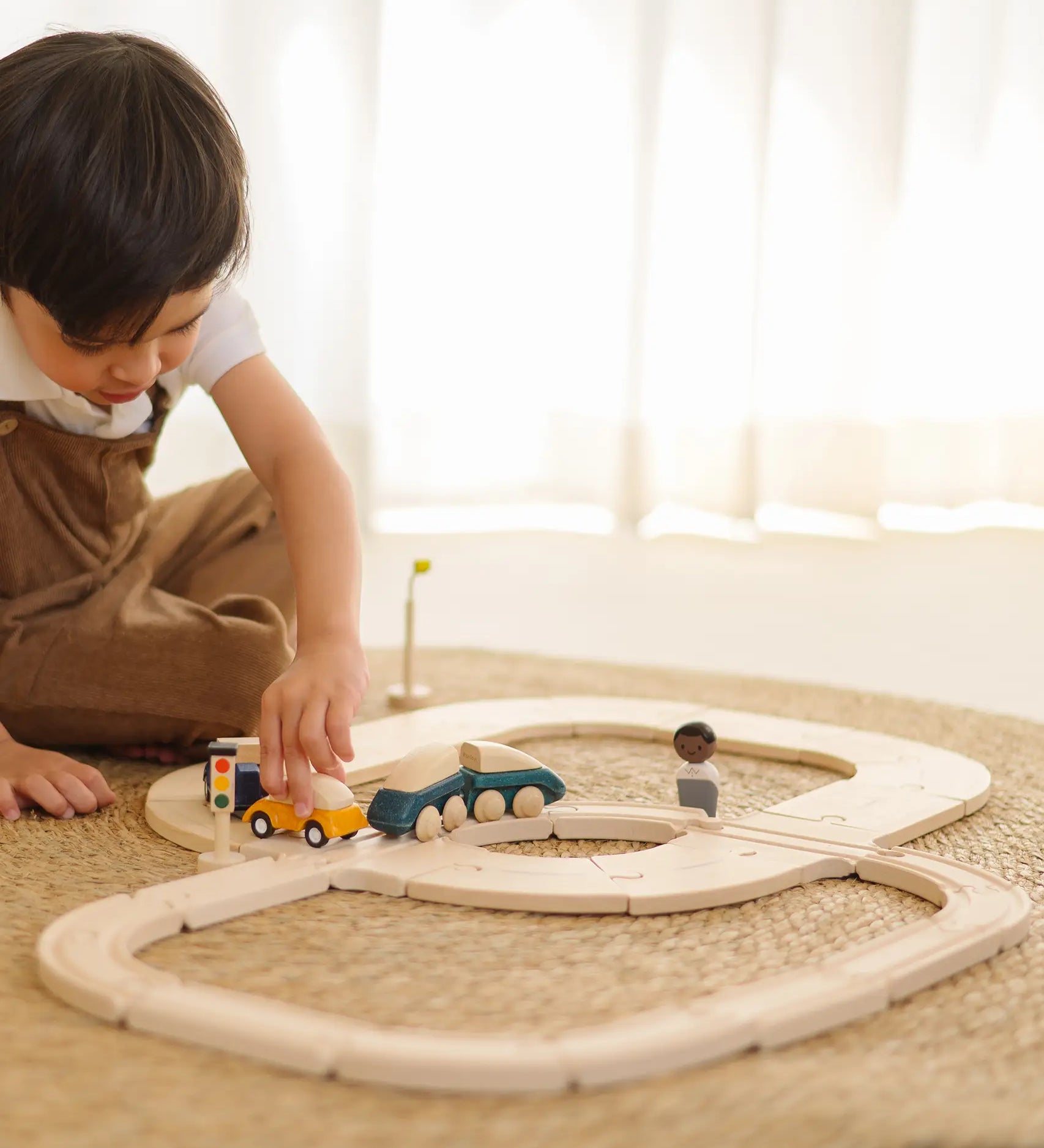 Child holding a yellow car on the wooden road piece from PlanToys  my first rail road playset