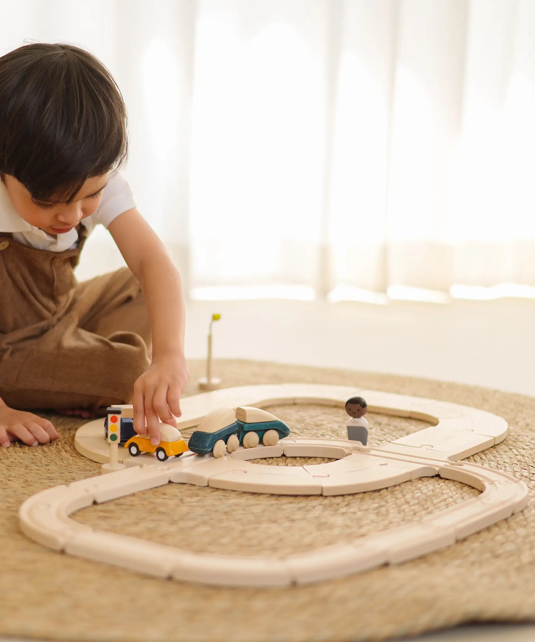 Child holding a yellow car on the wooden road piece from PlanToys  my first rail road playset