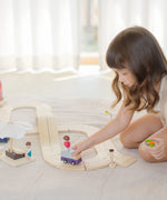 Child playing with a purple truck on the PlanToys wooden road pieces