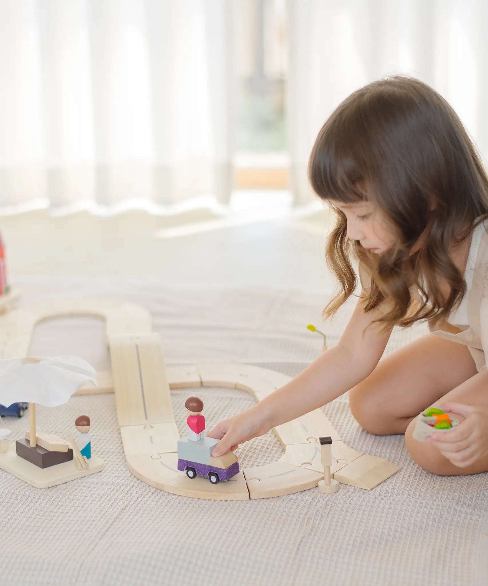 Child playing with a purple truck on the PlanToys wooden road pieces