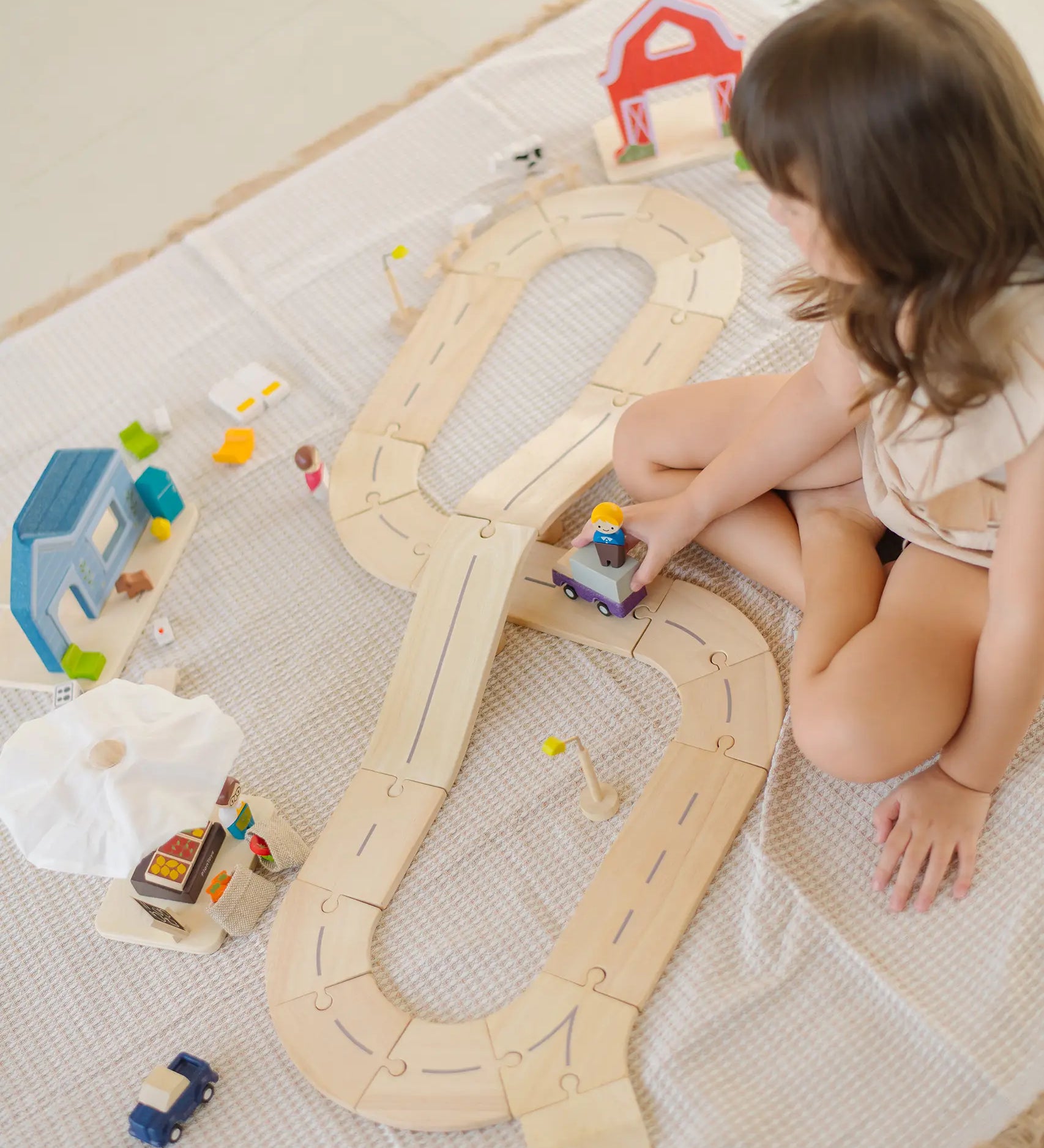 Child playing with the PlanToys my little wooden neighbourhood play set on a white blanket