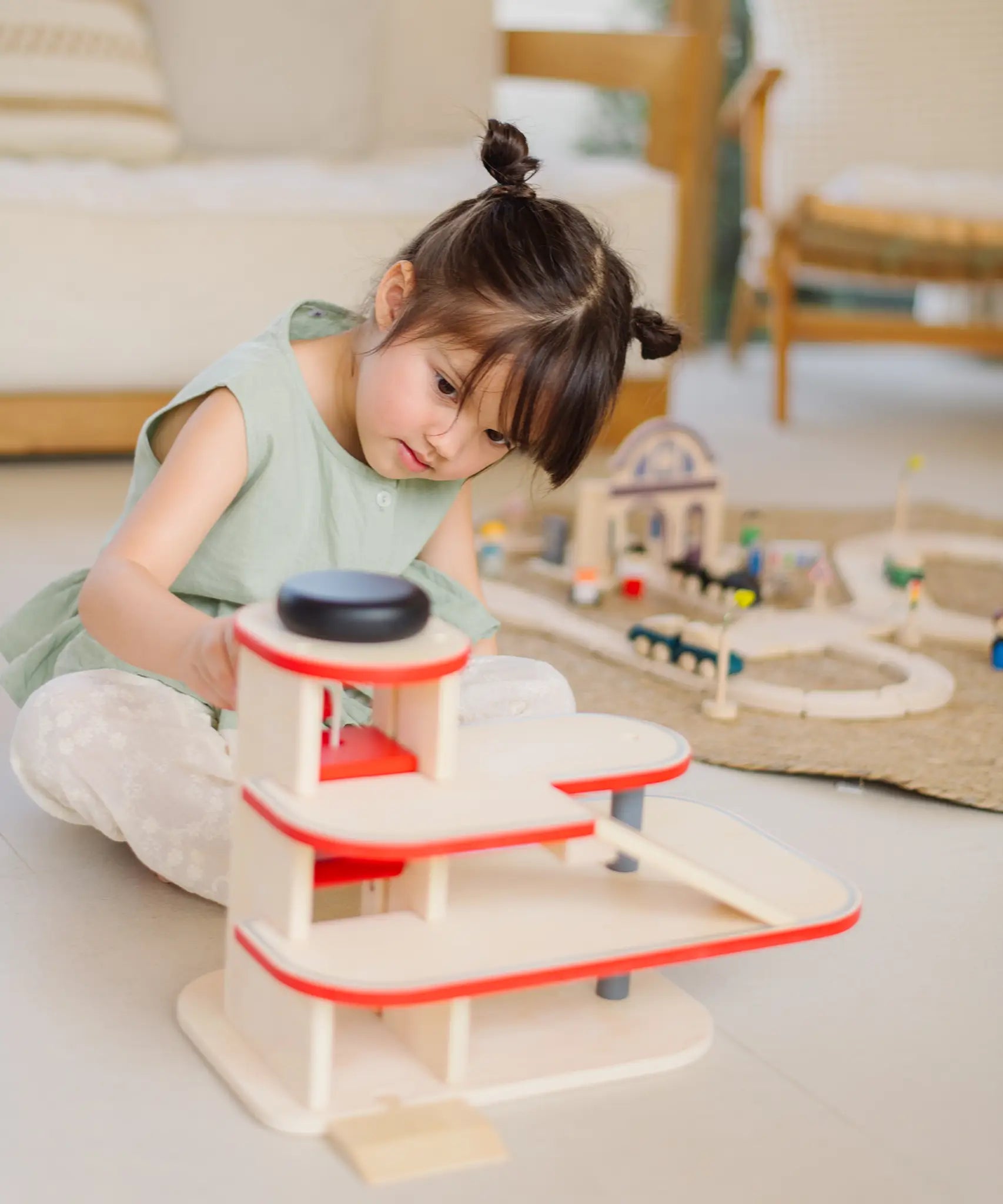 Child using the wind up lift on the PlanToys wooden city parking garage to move a vehicle