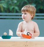 A child playing with a Plan Toys penguin Sailing Boat, there is a Plan Toys Polar Bear Sailing Boat next to him too. 