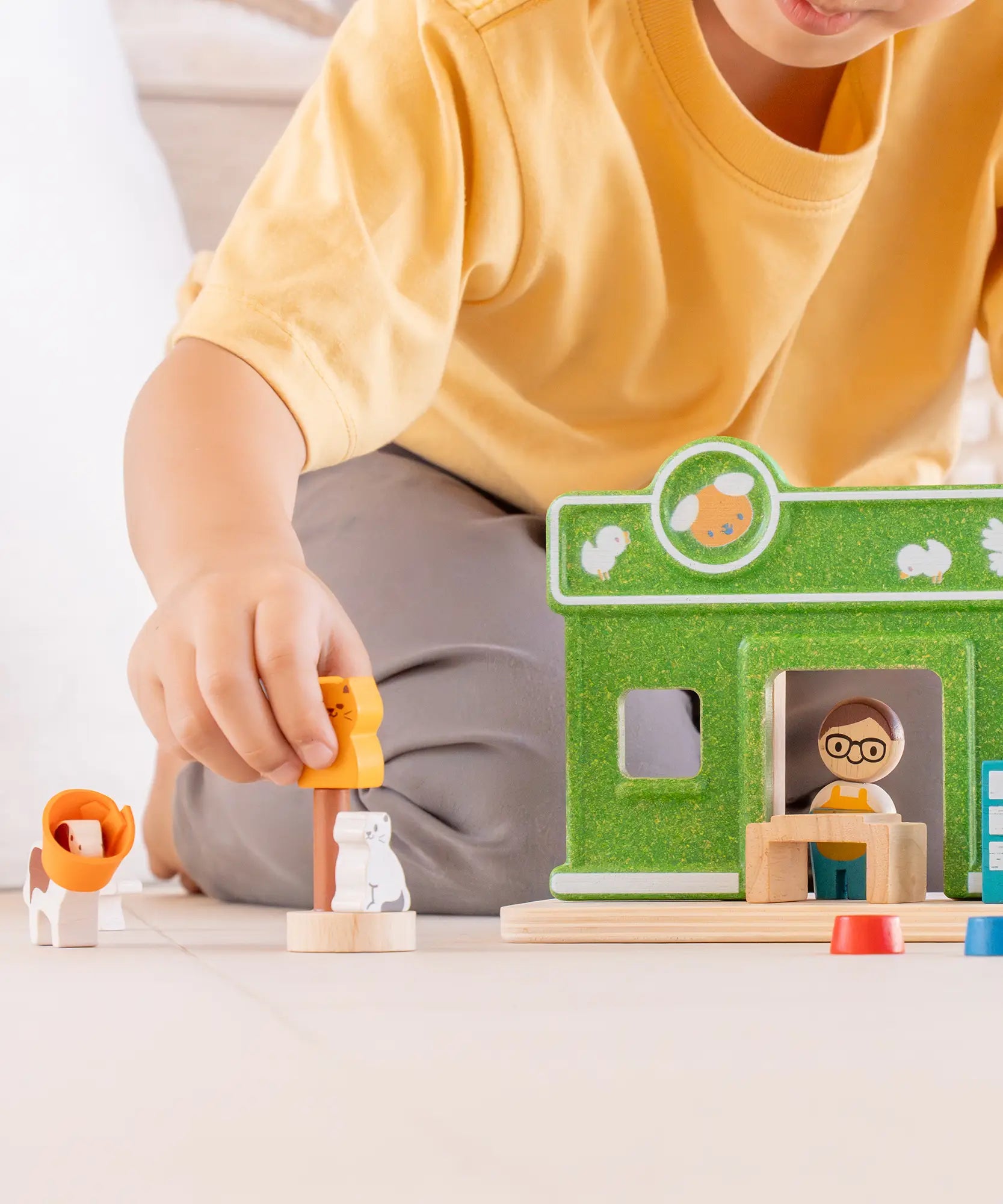 Child holding a cat figure next to a PlanToys pet shop play set showing scale