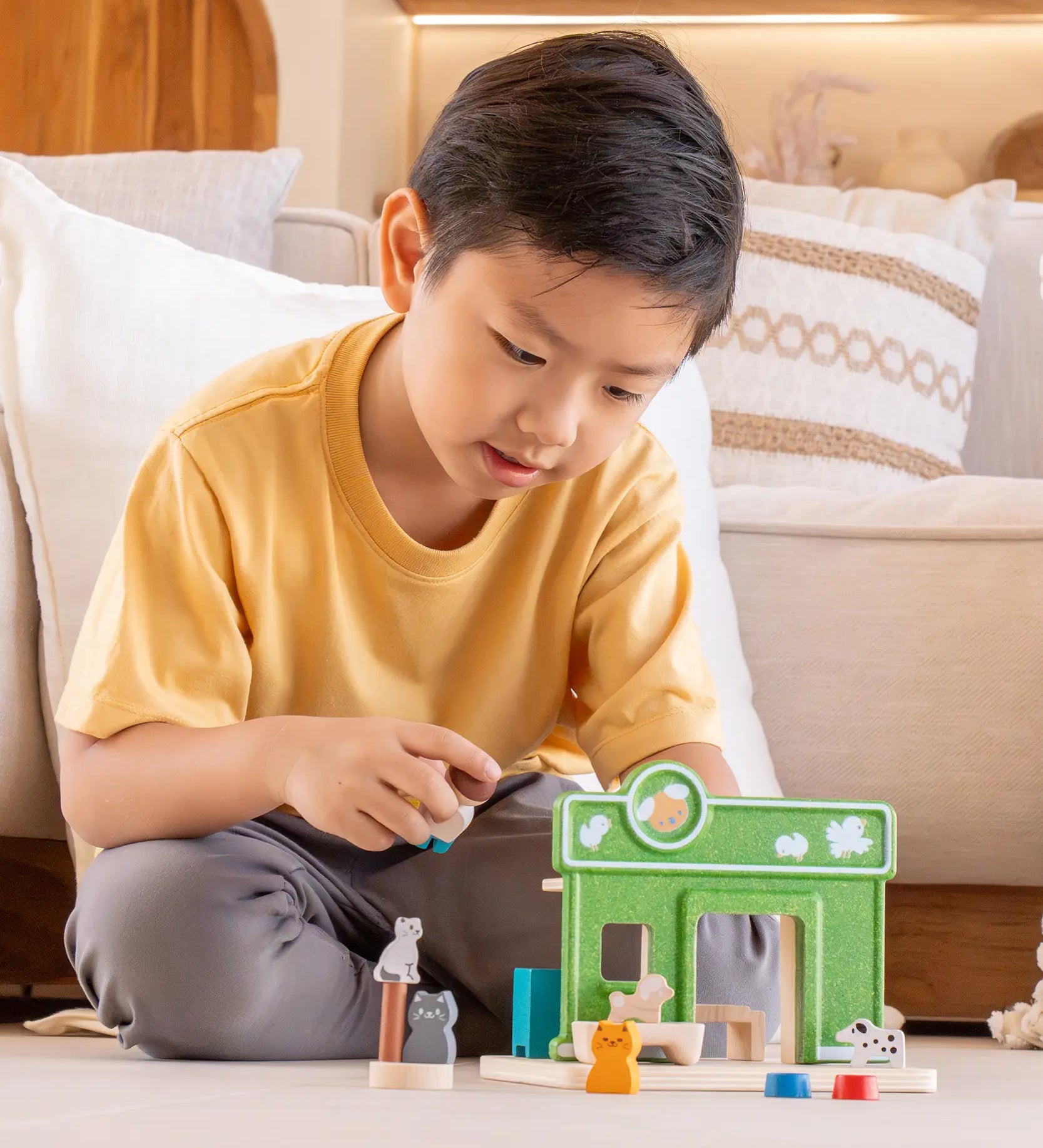Child holding a shop keeper figure next to a PlanToys pet shop play set showing scale 