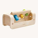 The peg board lifted up on the PlanToys Pounding Bench, to show the pegs going through the holes. Little wooden dowels allow the peg board to stay in place when hammering, and to move upwards to collect the pegs. The image is on a cream background