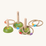 PlanToys Meadow Ring Toss, comes with 3 wooden pegs with green bases with flowers painted on them, and 6 rope rings with a different colour block on each ring. The image is on a cream background