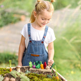 A PlanToys wooden seedling patch filled with loose play veg pieces with a child standing behind a large planter