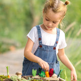 Child sorting loose wooden veg pieces on a PlanToys seedling planter piece in the garden