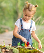 Child sorting loose wooden veg pieces on a PlanToys seedling planter piece in the garden
