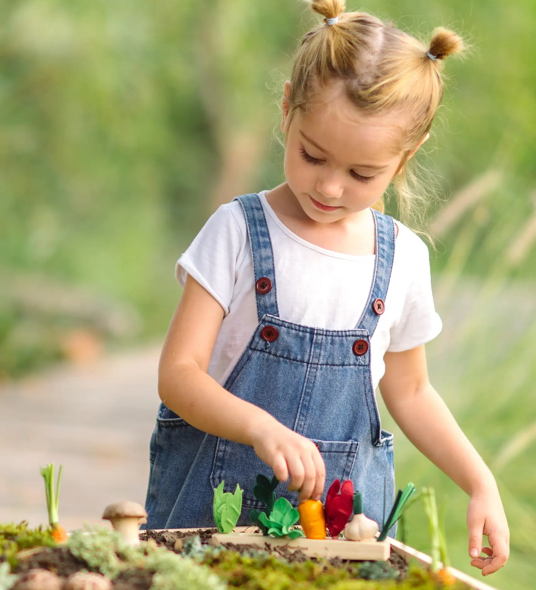 Child sorting loose wooden veg pieces on a PlanToys seedling planter piece in the garden