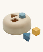 PlanToys Geometric Sorting toy, offers a fun and interactive experience for babies and little ones. Made from PlanWood, the shape sorting box has smooth, curved sides and three holes in the top. One of a square, a triangle and a circle. The circle block is in the circle hole, and the triange and square block are next to the shape sorter. The image is on a cream background