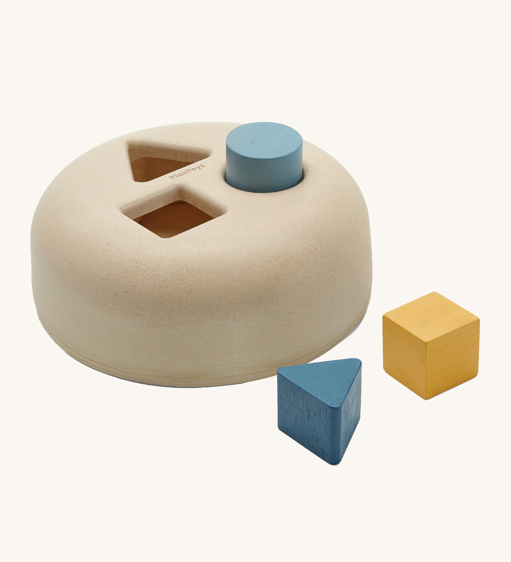 PlanToys Geometric Sorting toy, offers a fun and interactive experience for babies and little ones. Made from PlanWood, the shape sorting box has smooth, curved sides and three holes in the top. One of a square, a triangle and a circle. The circle block is in the circle hole, and the triange and square block are next to the shape sorter. The image is on a cream background