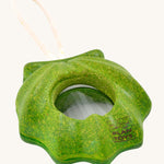 PlanToys Shell Kaleidoscope, is a green sensory kaleidoscope toy in the image of a shell, with a circular lens in the middle and a beige rope handle. The image is on a cream background 