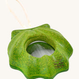 PlanToys Shell Kaleidoscope, is a green sensory kaleidoscope toy in the image of a shell, with a circular lens in the middle and a beige rope handle. The image is on a cream background 