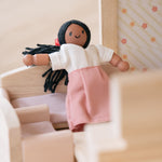 A doll shown sitting on the PlanToys Wooden sofa from the Living Room furniture set . 