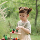 Child standing next to stacked planting beds from the PlanToys stack & sprout set with loose veg sitting on top