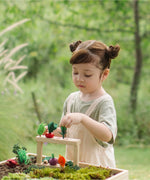 Child standing next to stacked planting beds from the PlanToys stack & sprout set with loose veg sitting on top