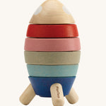 Plan Toys Wooden Stacking Rocket Orchard, has four coloured discs that make up the rocket, each with a cut out for a shape to go into, and a cute little astronaut who hides inside. The image is on a cream background
